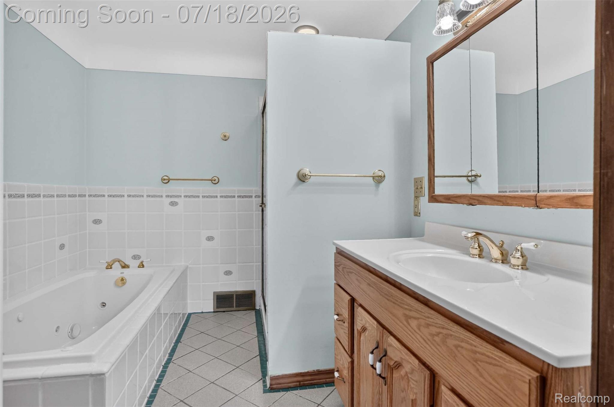 1437 East Cook Road Grand Blanc, MI 48439 - Photo 58 of 69 Bathroom featuring a jetted tub with tile surround, a wood-finish vanity with an integrated sink, a mirrored medicine cabinet, and light blue wall color