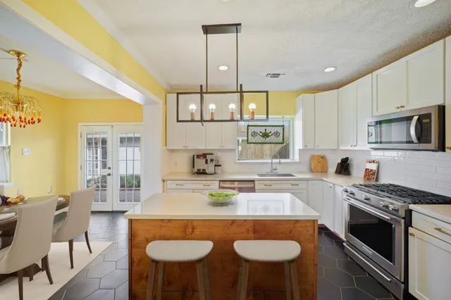 a kitchen with stainless steel appliances granite countertop a stove a sink a stove a kitchen island with chairs and white cabinets