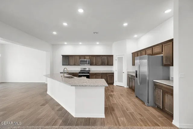 a kitchen with stainless steel appliances kitchen island granite countertop a stove a refrigerator a oven with white cabinets and wooden floor