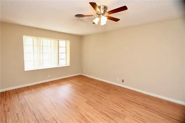 an empty room with wooden floor fan and windows
