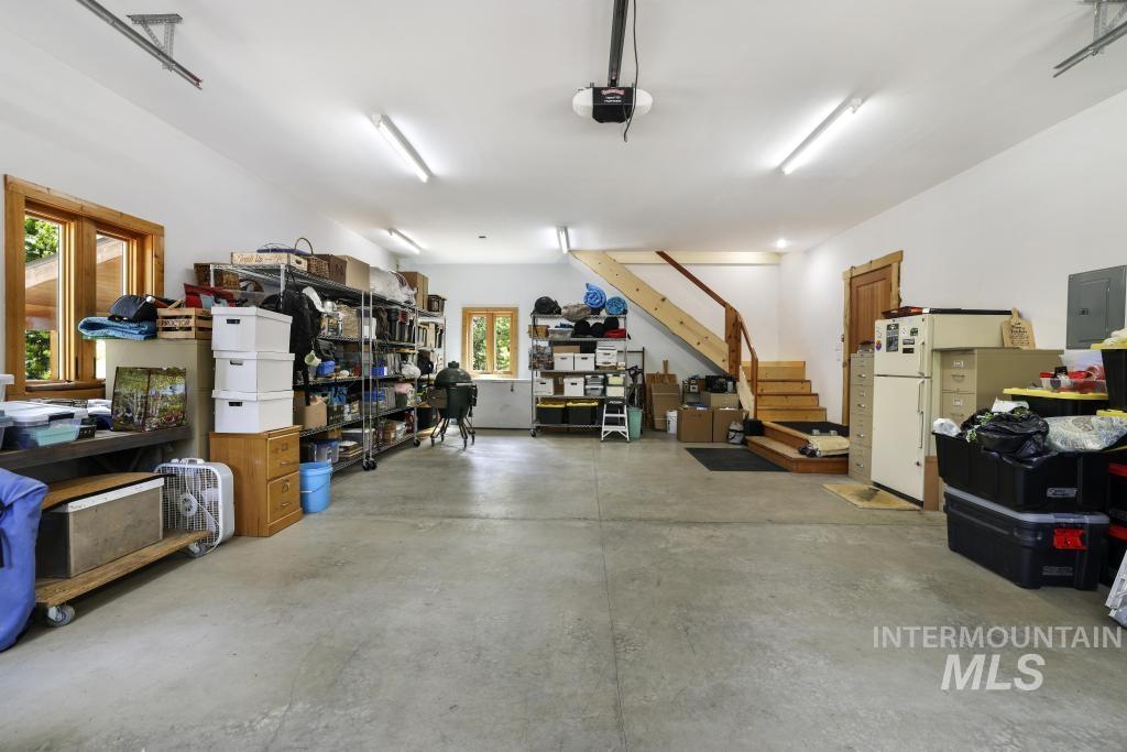65 Goat Creek Way Stanley, ID 83278 - Photo 28 of 32 Spacious garage featuring a concrete floor, multiple windows with wood trim, fluorescent lighting, and a wood staircase