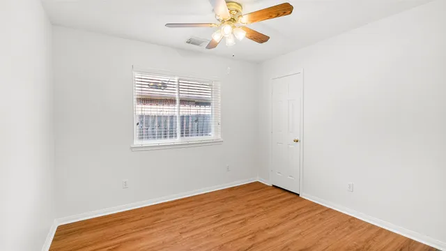 a view of empty room with wooden floor and fan