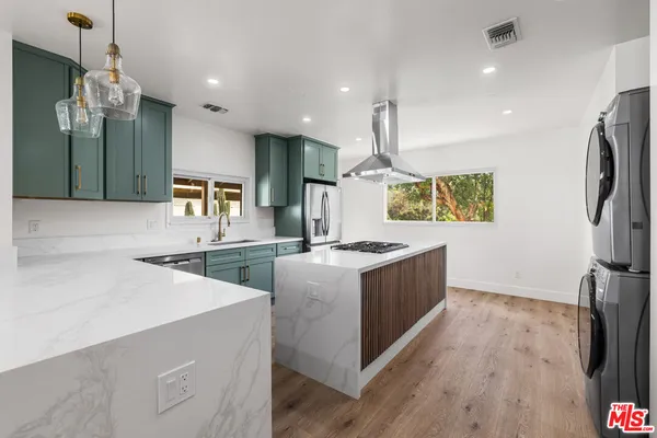 a large kitchen with stainless steel appliances a large counter top a stove a sink and a refrigerator