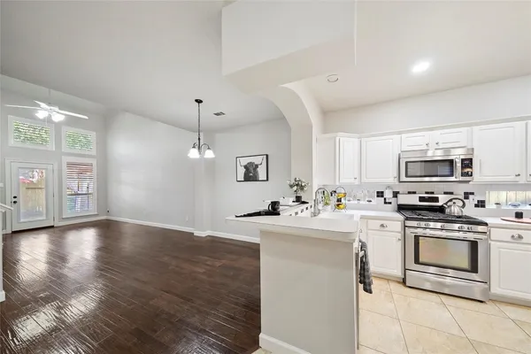 a kitchen with stainless steel appliances a stove top oven a sink a refrigerator white cabinets and wooden floor
