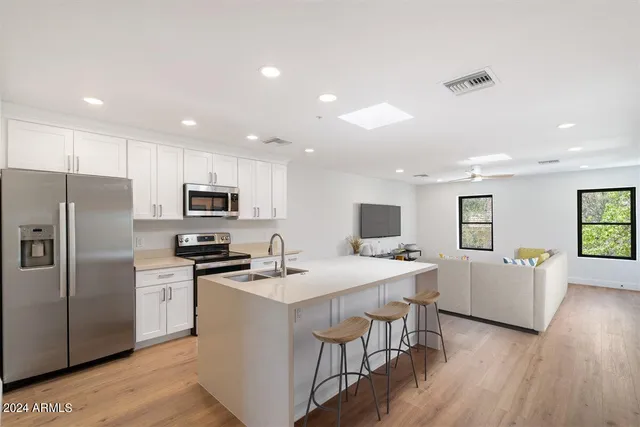 a kitchen with stainless steel appliances a microwave a stove a sink a refrigerator and white cabinets with wooden floor