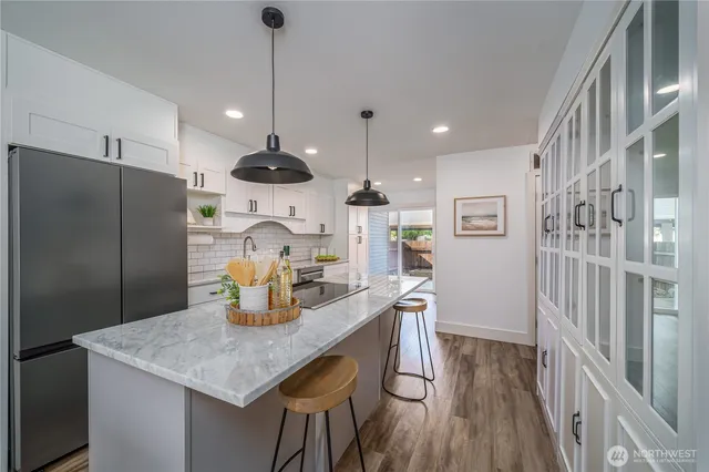 a kitchen with stainless steel appliances granite countertop a refrigerator a sink dishwasher a dining table and chairs with wooden floor