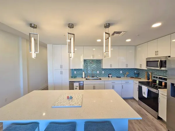 a large kitchen with stainless steel appliances a stove a sink dishwasher a refrigerator and white cabinets with wooden floor