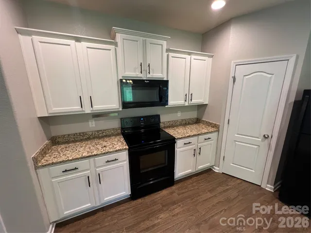 a kitchen with granite countertop white cabinets and black appliances