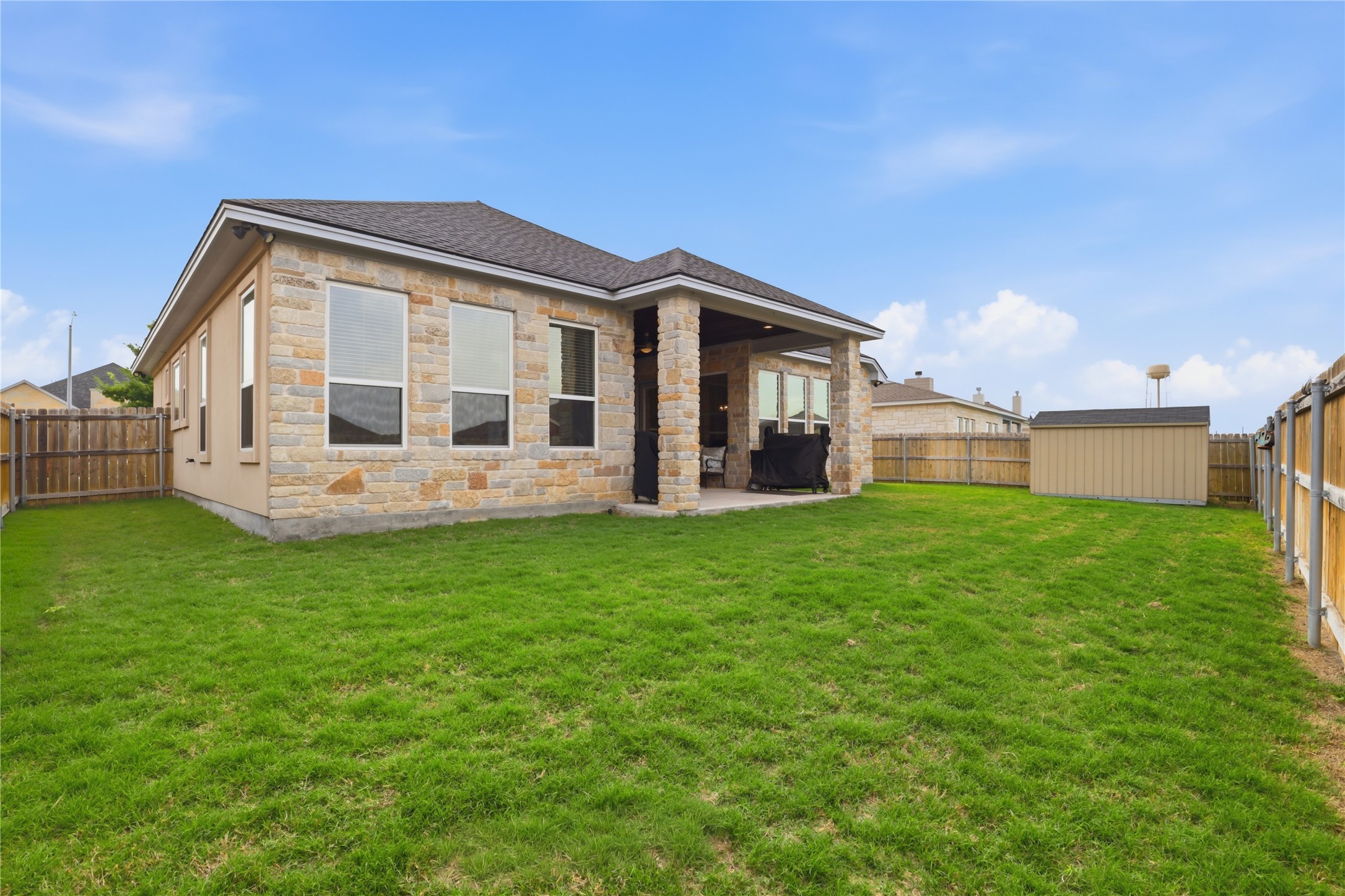 133 Greg Lane Jarrell, TX 76537 - Photo 23 of 24 Expansive grassy backyard featuring a covered patio, stone exterior, multiple windows, and a detached storage shed