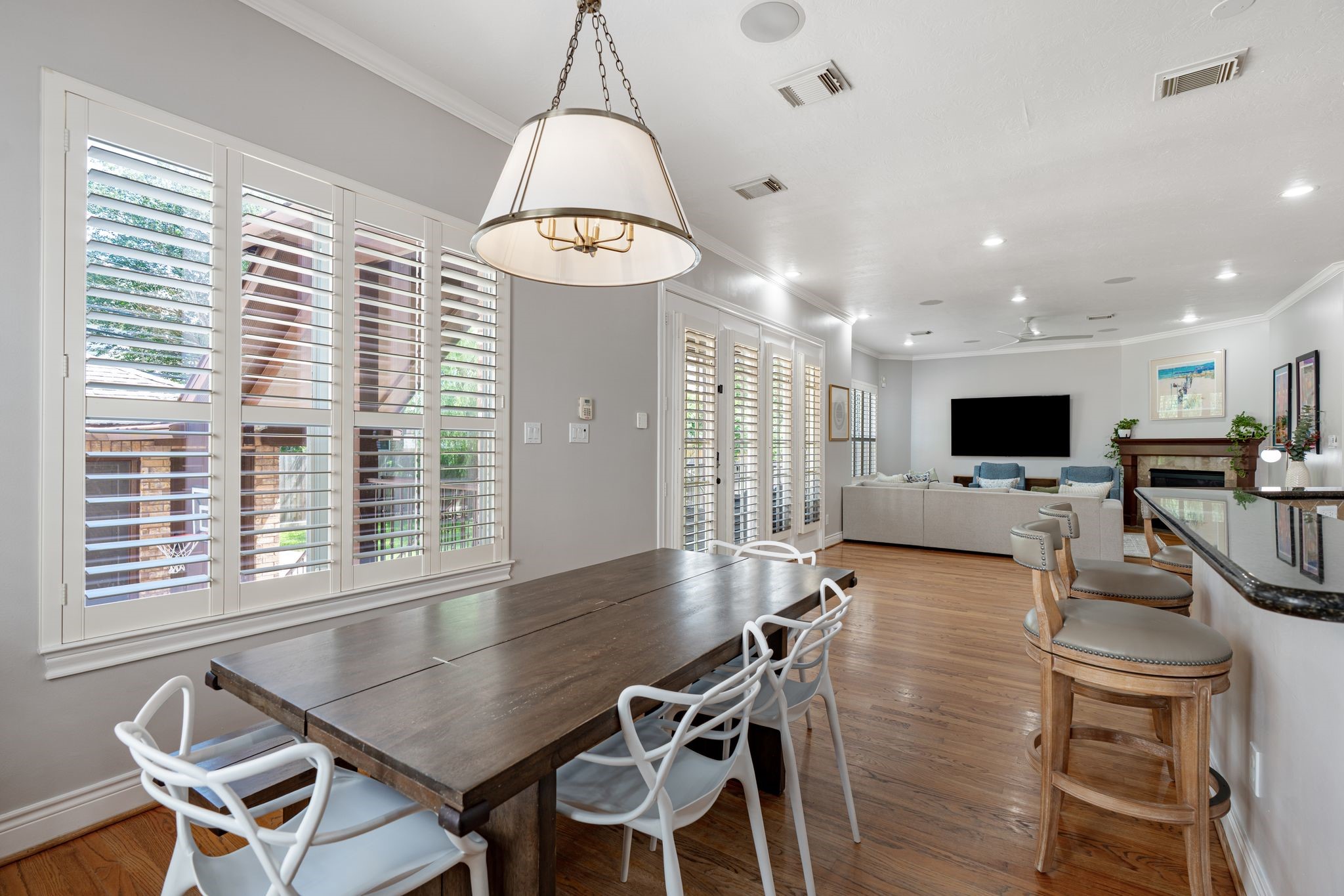 3822 Merrick Street Houston, TX 77025 - Photo 12 of 34 From the breakfast nook, a wall of plantation shutters and French doors leads out to the backyard, while the view into the family room — with the fireplace and built-in media wall — reinforces the home's open, connected layout. The granite-topped bar counter is visible to the right.
