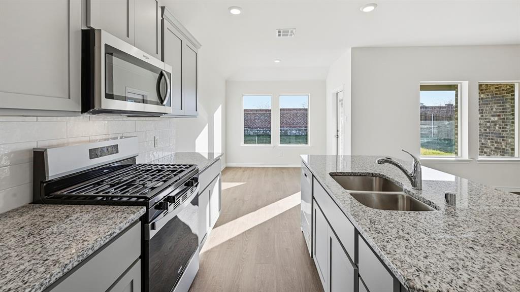 419 Epiphany Lane Lavon, TX 75166 - Photo 7 of 31 Kitchen featuring granite countertops, stainless steel appliances, grey cabinetry, a white subway tile backsplash, and wood-finish flooring