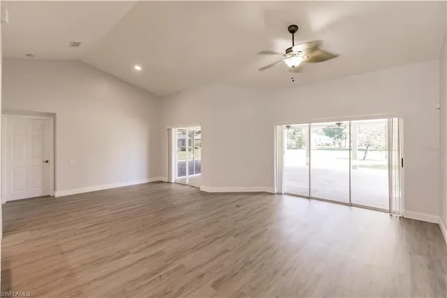 an empty room with wooden floor fan and windows