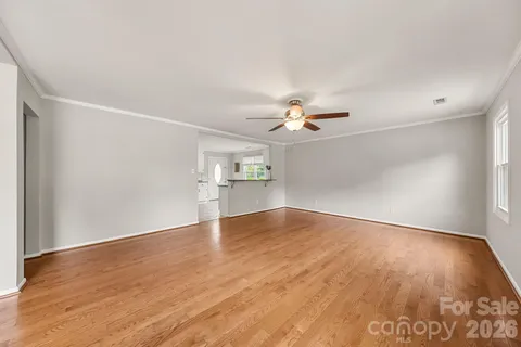 an empty room with wooden floor chandelier fan and windows