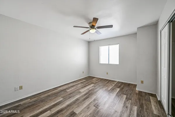 an empty room with wooden floor ceiling fan and windows