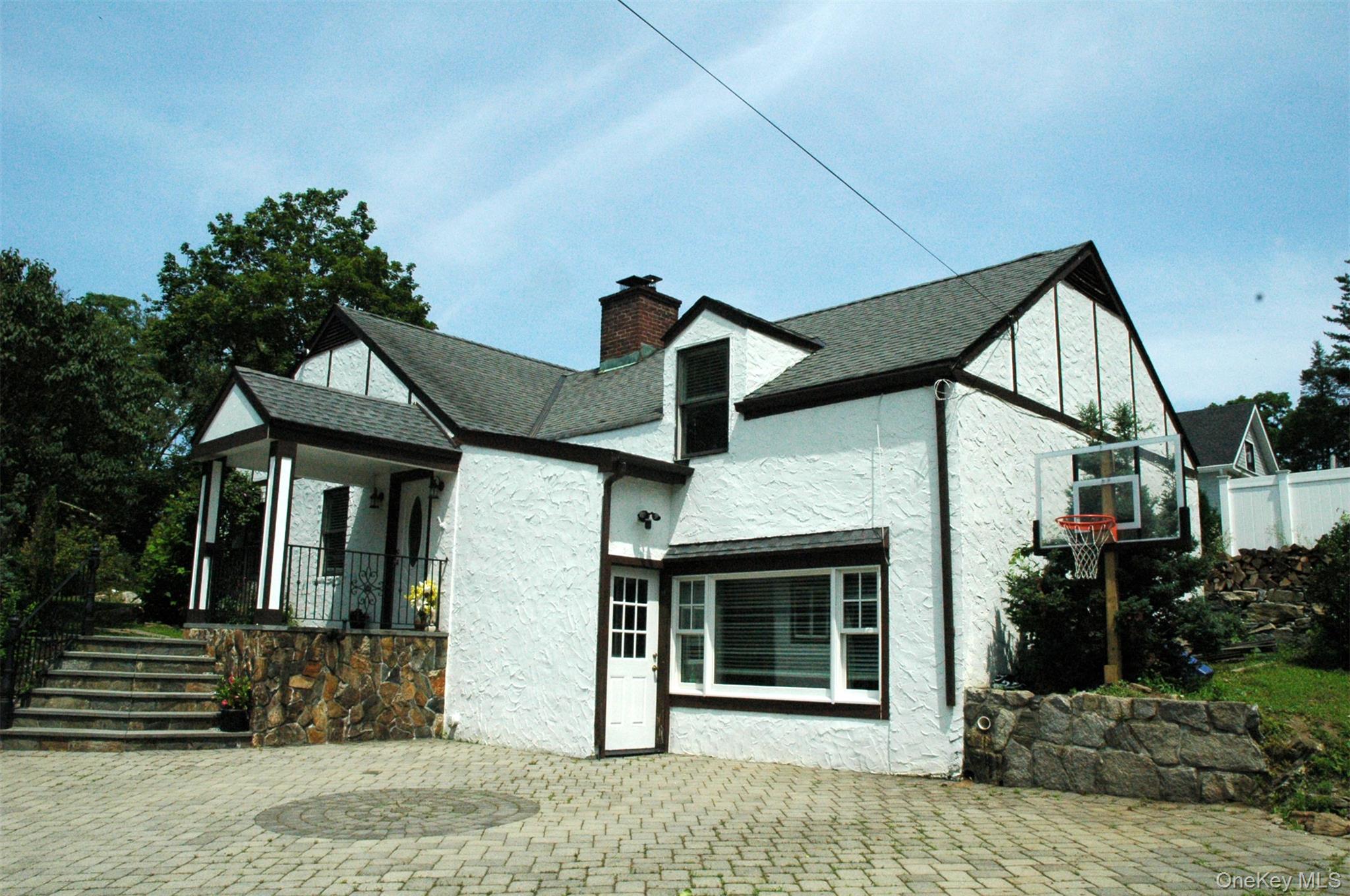 Back of property featuring a chimney, stucco siding, a patio area, a shingled roof, and covered porch