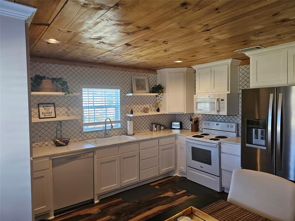 165 Elmwood Road Whitney, TX 76692 - Photo 12 of 28 Kitchen with open shelves, white appliances, wood ceiling, white cabinetry, and tasteful backsplash