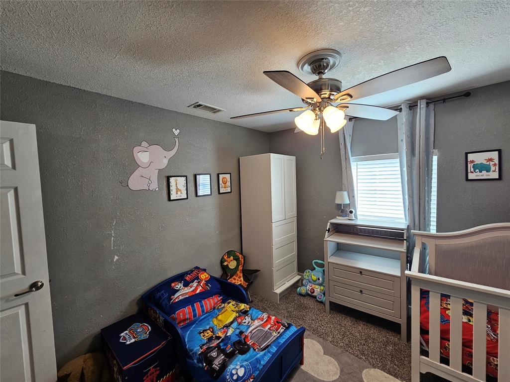 165 Elmwood Road Whitney, TX 76692 - Photo 24 of 28 Bedroom with a textured wall, a textured ceiling, a ceiling fan, and dark colored carpet