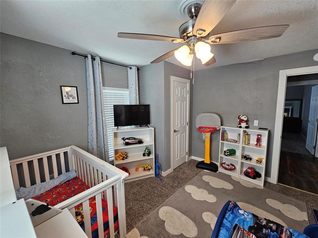 165 Elmwood Road Whitney, TX 76692 - Photo 25 of 28 Bedroom featuring a nursery area, ceiling fan, a textured ceiling, carpet flooring, and a textured wall