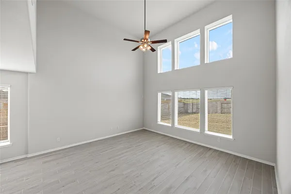 an empty room with wooden floor ceiling fan and windows