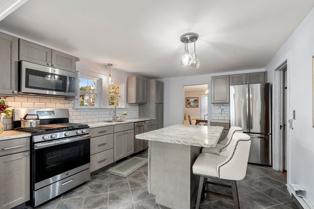 17 Centre Lane Milton, MA 02186 - Photo 7 of 26 a kitchen with stainless steel appliances granite countertop a stove top oven a sink dishwasher a dining table and chairs with wooden floor