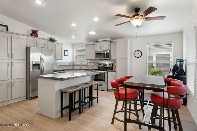 a kitchen with stainless steel appliances kitchen island granite countertop a dining table chairs refrigerator and microwave