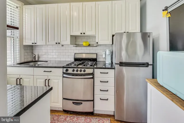 a kitchen with granite countertop a refrigerator stove and white cabinets