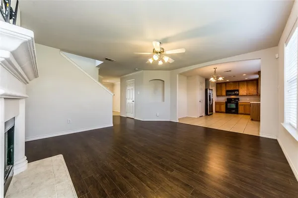 a view of an empty room with wooden floor and a kitchen