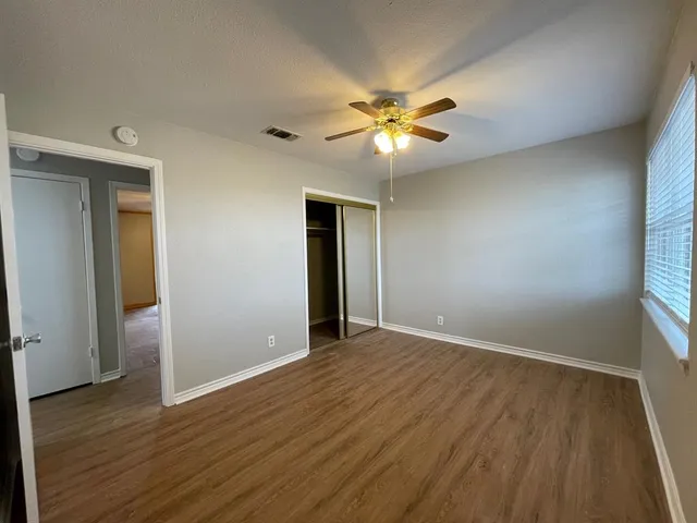 an empty room with wooden floor fan and windows