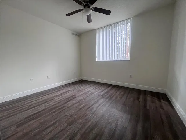 an empty room with wooden floor ceiling fan and windows