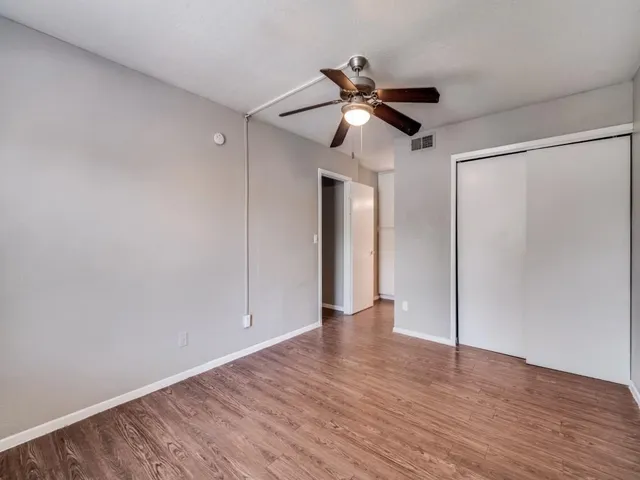 a view of an empty room with wooden floor and a ceiling fan