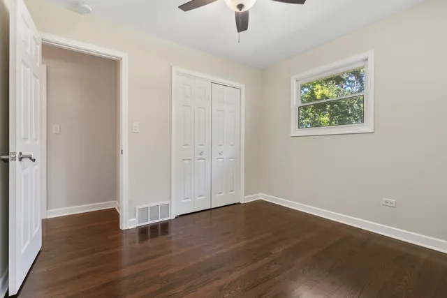 an empty room with wooden floor chandelier fan and windows
