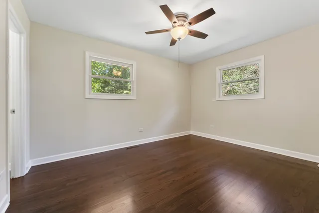 a view of an empty room with wooden floor and a ceiling fan