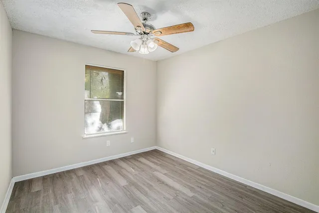 an empty room with wooden floor fan and windows