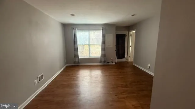an empty room with wooden floor and windows with curtains