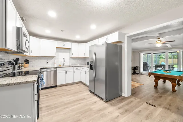 a kitchen with stainless steel appliances granite countertop a refrigerator a sink dishwasher a stove with white cabinets and wooden floor