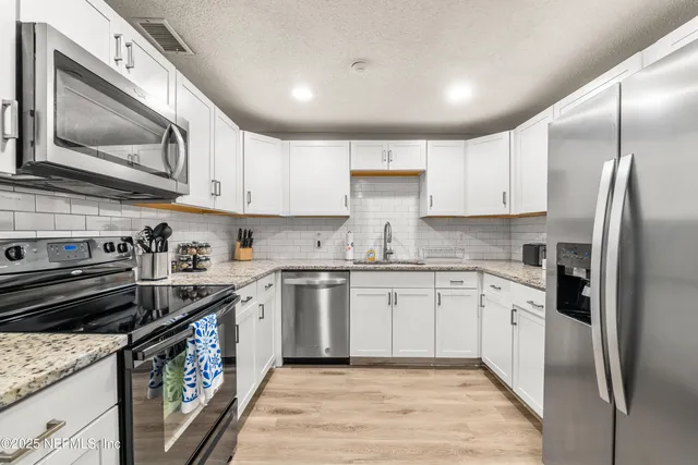 a kitchen with stainless steel appliances granite countertop a stove top oven a sink and dishwasher a refrigerator with wooden floor