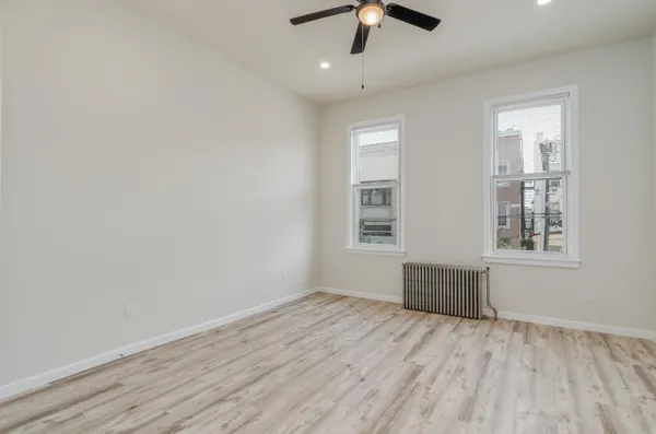 an empty room with wooden floor chandelier fan and windows