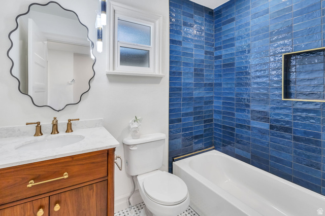 226 North 300 West Provo, UT 84601 - Photo 9 of 14 Bathroom featuring a white bathtub with a blue tiled surround, built-in shelving niche, wood-finish vanity with a white countertop, and brass-finish fixtures