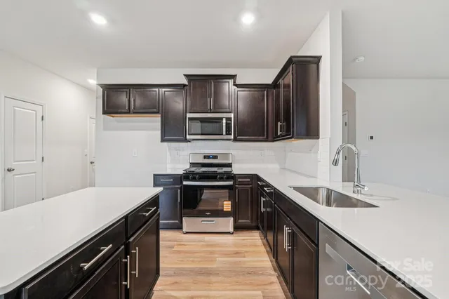 a kitchen with stainless steel appliances a sink dishwasher a stove top oven a refrigerator with wooden floors