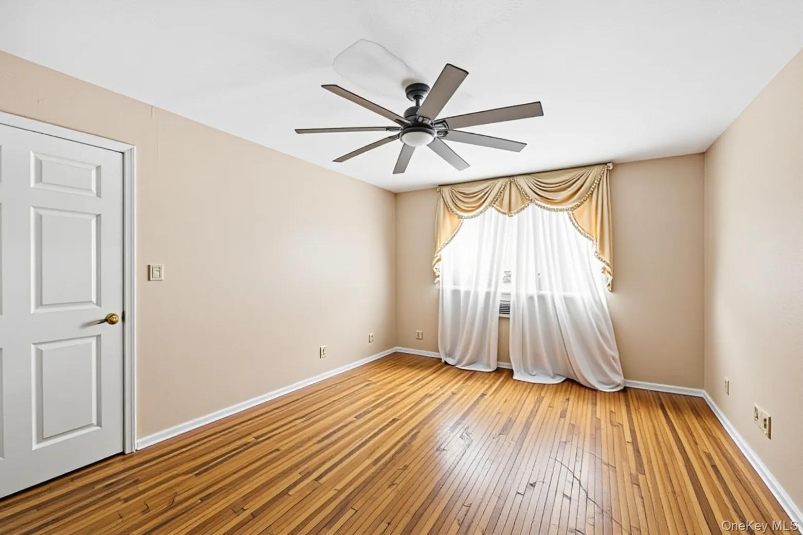 49-12 111th Street Queens, NY 11368 - Photo 12 of 31 an empty room with wooden floor fan and windows