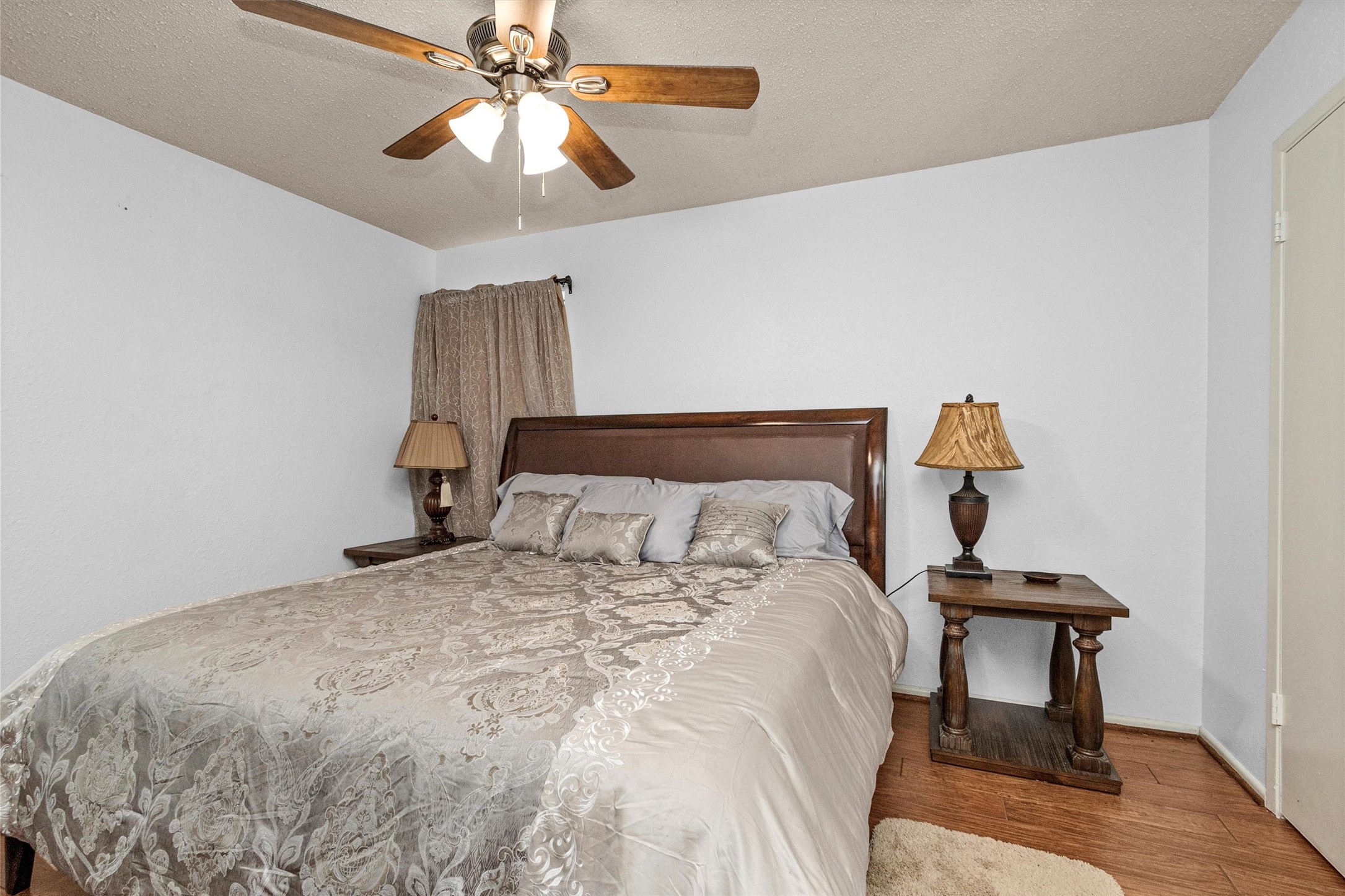 12900 Walden Road, Unit D 411 Montgomery, TX 77356 - Photo 12 of 18 Discover tranquility in this cozy bedroom, featuring a large bed with elegant bedding, warm wood flooring, and wooden nightstands with lamps, all under the gentle breeze of a ceiling fan and the calm embrace of neutral walls.