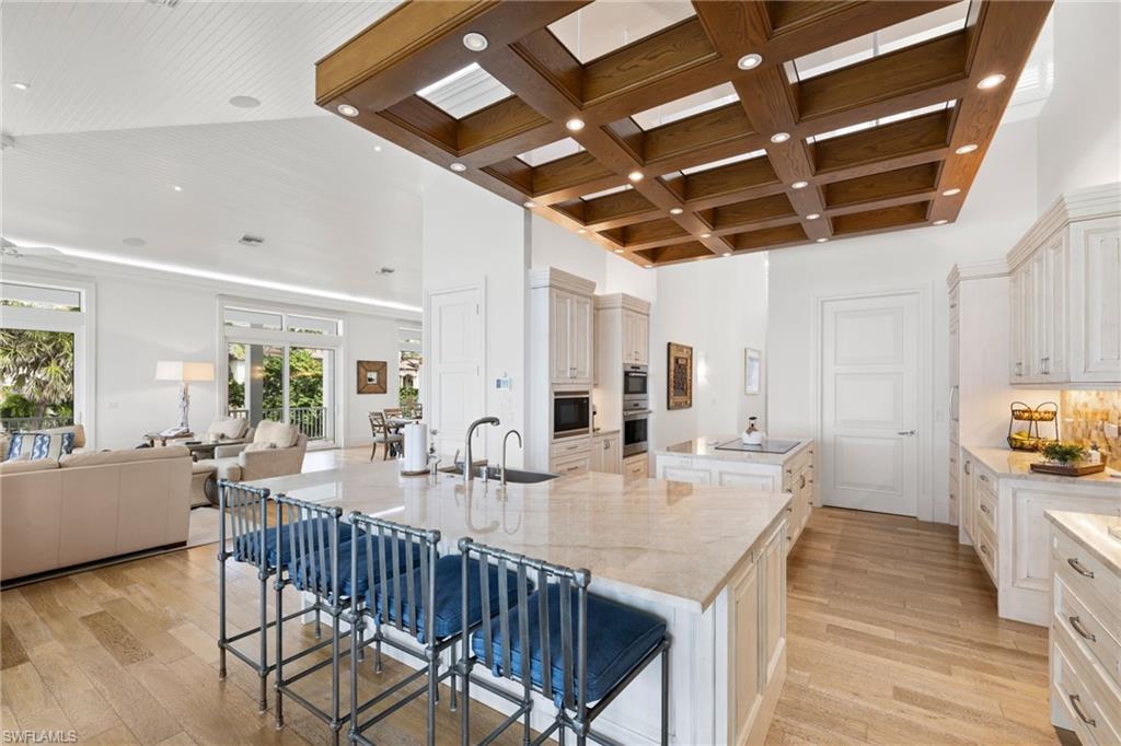 40 32nd Avenue South Naples, FL 34102 - Photo 49 of 49 Kitchen featuring light wood-type flooring, a kitchen breakfast bar, open floor plan, light stone counters, and coffered ceiling