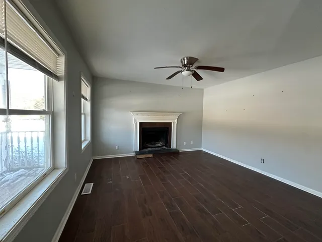 an empty room with wooden floor fan and windows