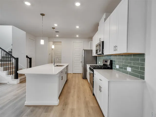 a kitchen with stainless steel appliances kitchen island hardwood floor sink stove and white cabinets
