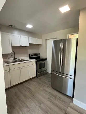 a kitchen with granite countertop stainless steel appliances a refrigerator a sink and white cabinets