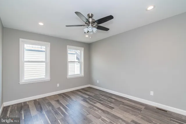 an empty room with wooden floor a ceiling fan and windows