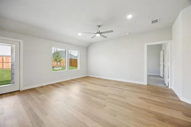 an empty room with wooden floor ceiling fan and windows