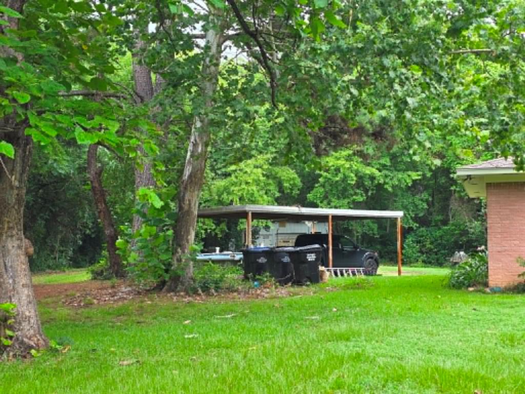 4514 West Loop 281 Longview, TX 75604 - Photo 6 of 36 Detached carport structure, mature trees, green lawn, and partial brick exterior