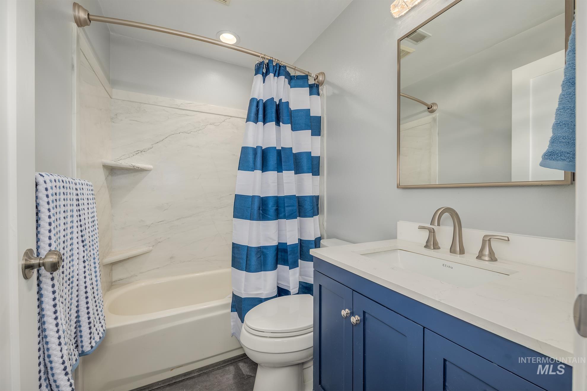 748 Pringle Road Weiser, ID 83672 - Photo 29 of 47 Bathroom featuring a white tub with a white-veined surround, a toilet, a blue vanity with a white countertop and integrated sink, a brushed nickel faucet, and a rectangular mirror with a brushed nickel frame