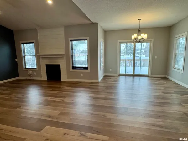 an empty room with wooden floor fireplace and windows